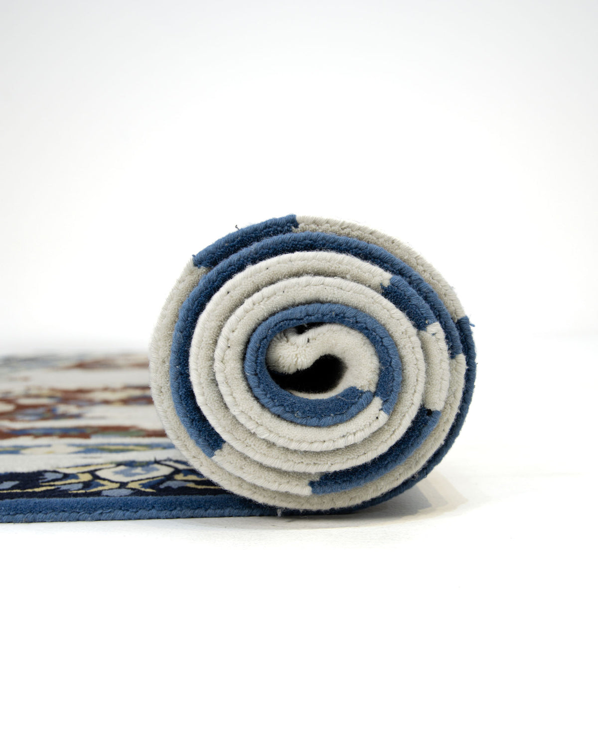 A rolled-up RAMSHA HOME Multi Color Handmade Area Rug - HTW 111 (300x400 cm) with blue and white edges, partially unrolled on a white surface, showing a hint of its pattern along the left edge.