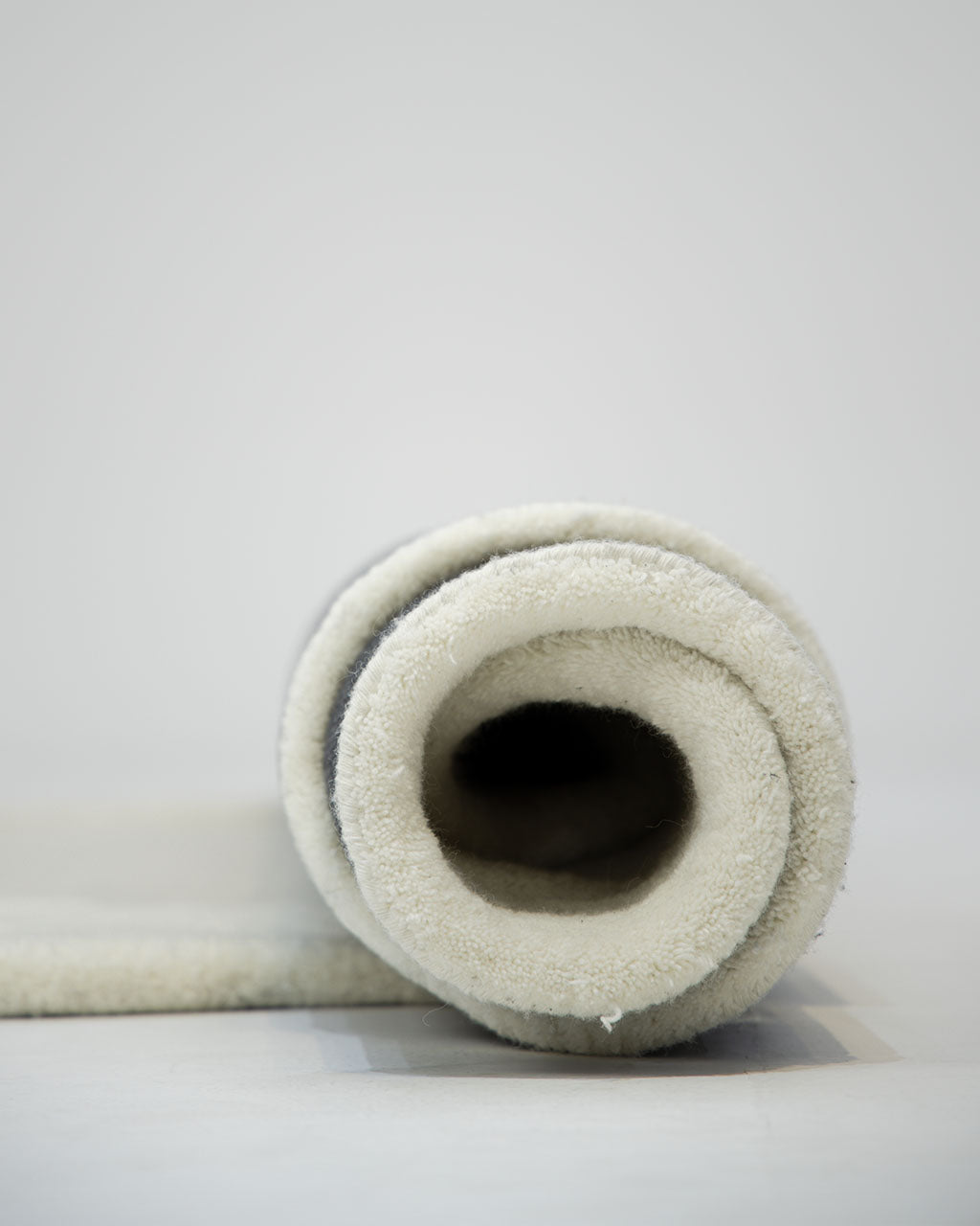 A close-up of a rolled-up RAMSHA HOME Handmade Shape White Color Area Rug - HTW 101 B displayed on a light surface with a plain background.