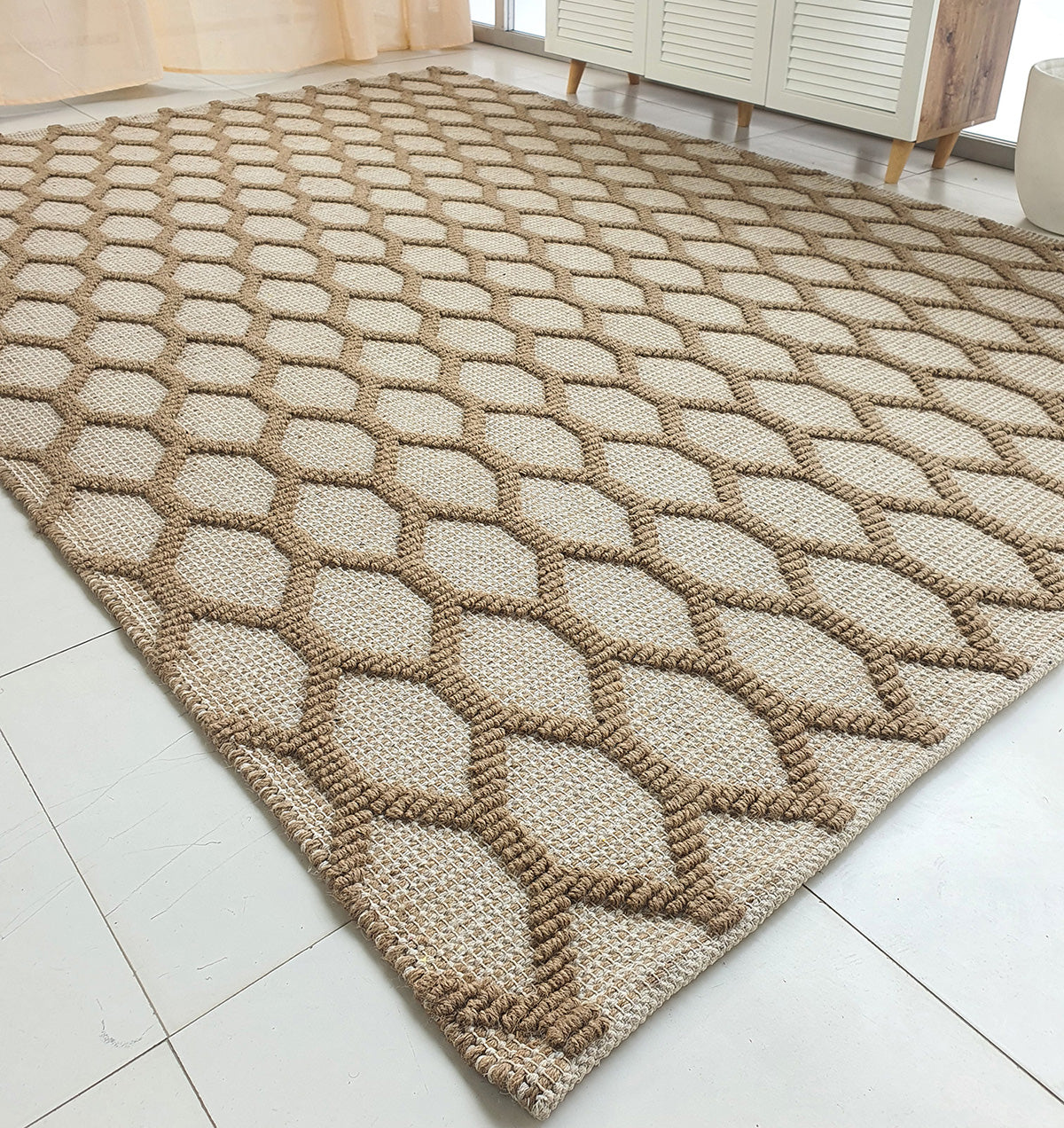 The RAMSHA HOME Rectangle Woven Area Rug Neutral Beige And Brown SR-023, featuring a geometric diamond pattern, is placed on light tile flooring in a modern room with minimal furniture.