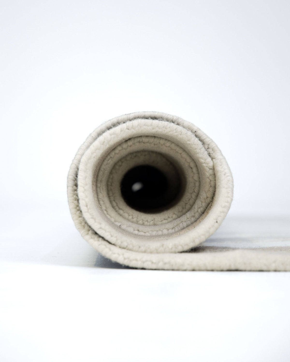 A close-up view of the RAMSHA HOME Beige & Cream Wavy Handmade Area Rug – HTWV-144, hand-tufted in viscose, rolled up tightly to reveal its circular layers from the side against a plain white background.