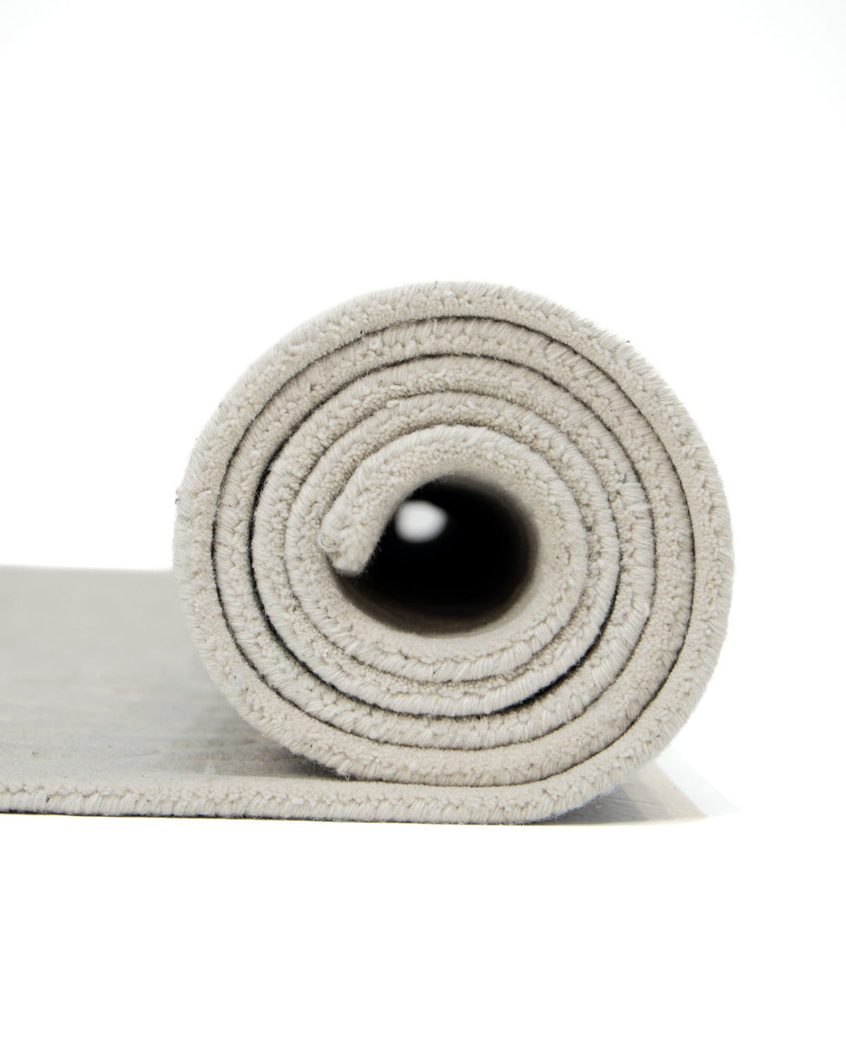 Close-up of a rolled-up light gray yoga mat, viewed from the side against a white background, with the RAMSHA HOME Rectangle Shape Beige Color Handmade Area Rug - HTW 132 (200x300 cm) adding subtle texture and warmth to the scene.