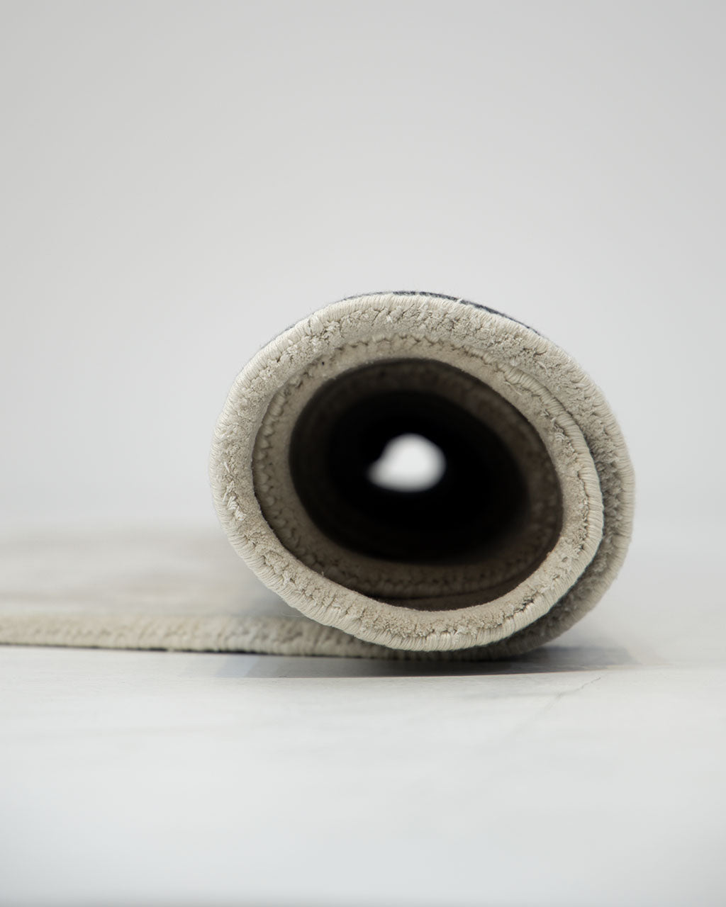 A close-up view of the rolled-up RAMSHA HOME Handmade Irregular 200x300 cm Rug HTWV-198, displayed on a flat surface against a white background.