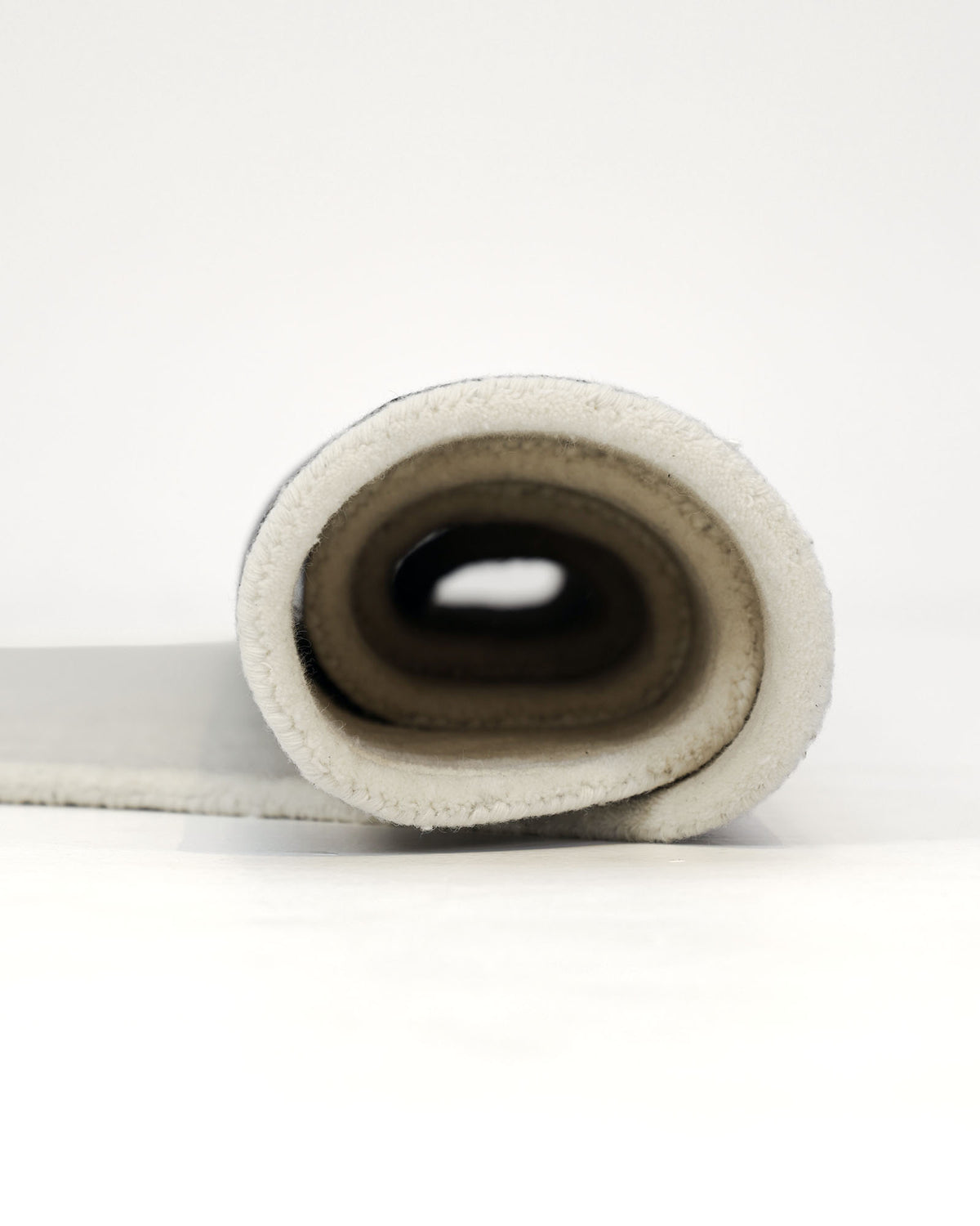 A close-up of the RAMSHA HOME Natural White Color Area Carpet - HTW 88, rolled up to showcase its soft, textured edge and subtle layered design in a modern neutral tone, all set against a plain white background.