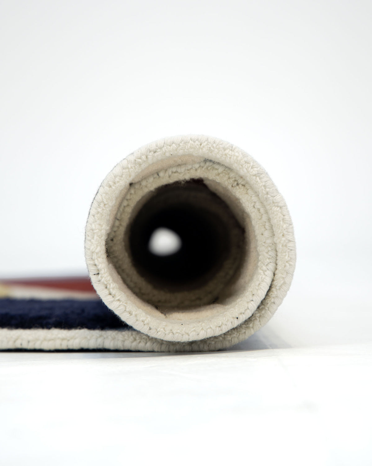 A close-up view of the RAMSHA HOME Handmade Wool & Cotton Abstract Round Area Rug HTW 125 (200cm), featuring a thick, light-colored edge, rolled up and positioned horizontally on a white surface.