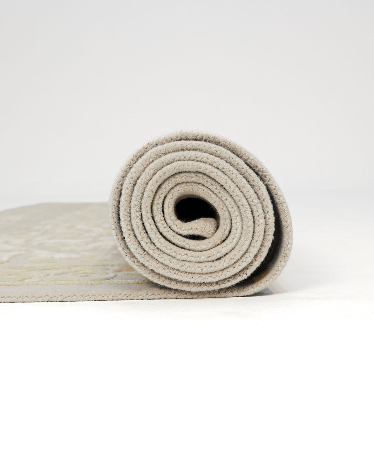 The RAMSHA HOME Handmade Beige Area Rug 300x400 cm (HTWV-56) is partially rolled up on a white surface, revealing its plush thickness and soft texture. The plain, minimalistic background accentuates the timeless appeal of this traditional rug.