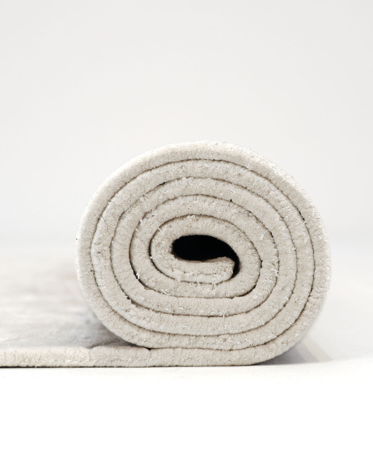 A neatly rolled-up RAMSHA HOME Rectangle Shape Beige Color Handmade Area Rug - HTV 25 (200x300 cm) is positioned on a white surface, with its spiral layers clearly visible in a front-facing photograph.