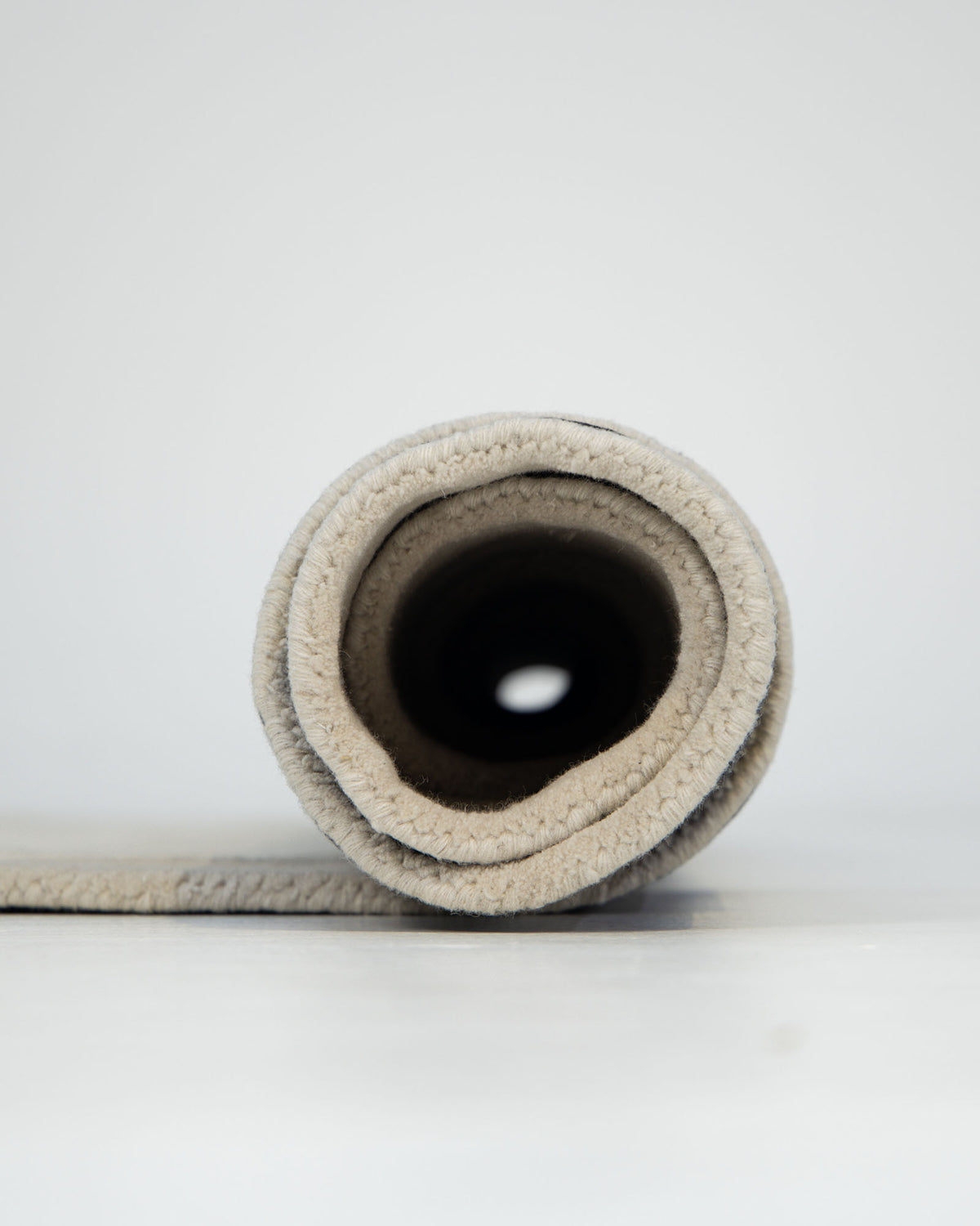 A close-up view of the RAMSHA HOME Wool & Tencel Multi Color Rug HTWV-91, hand-tufted and rolled up on a white surface, showcasing its inner spiral and soft texture against a plain light background.