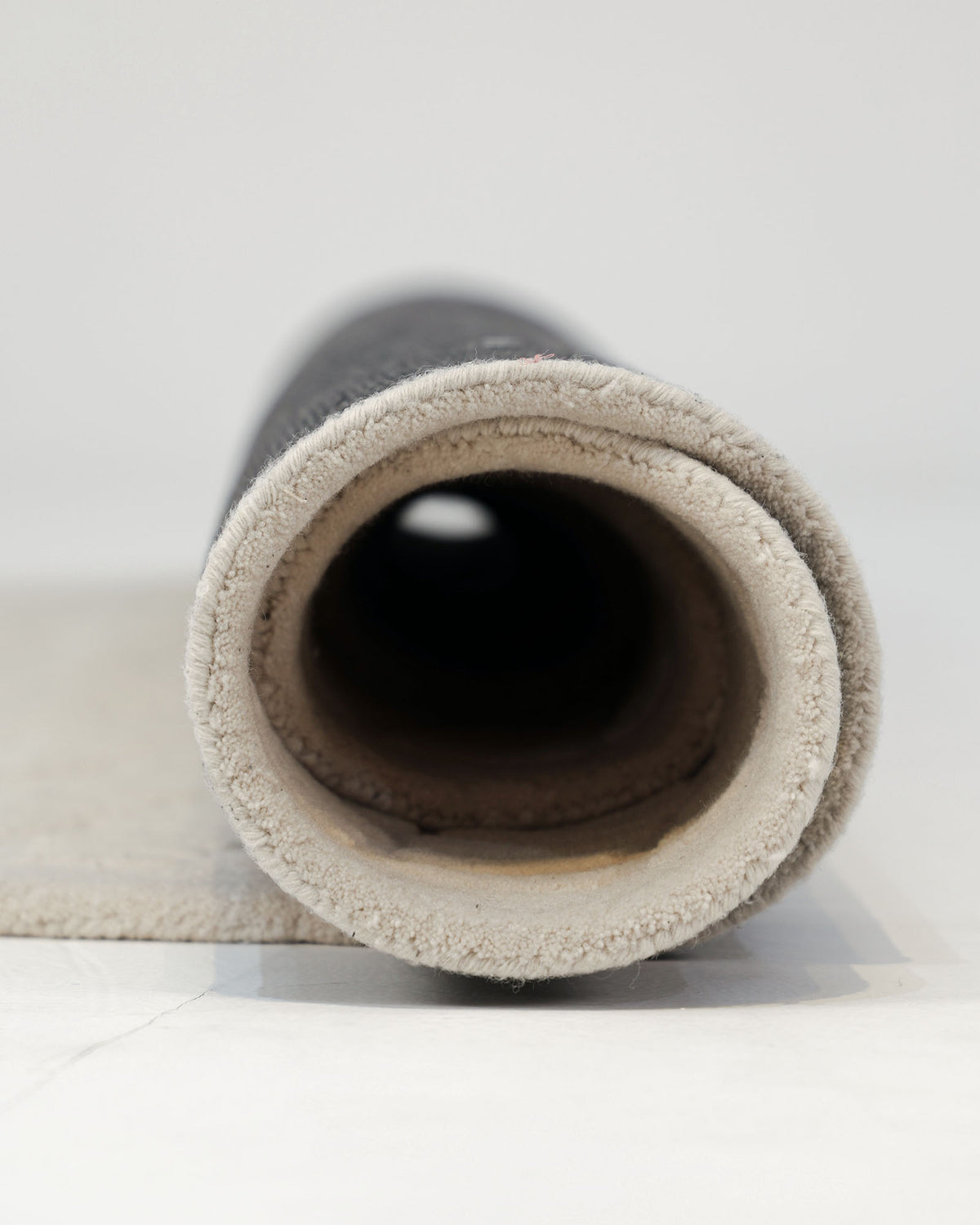 A close-up view of the RAMSHA HOME Beige Color Shape Handmade Rug HTW 104, rolled up to showcase its modern beige and gray textured design, lying on a light-colored floor with the open end facing the camera.
