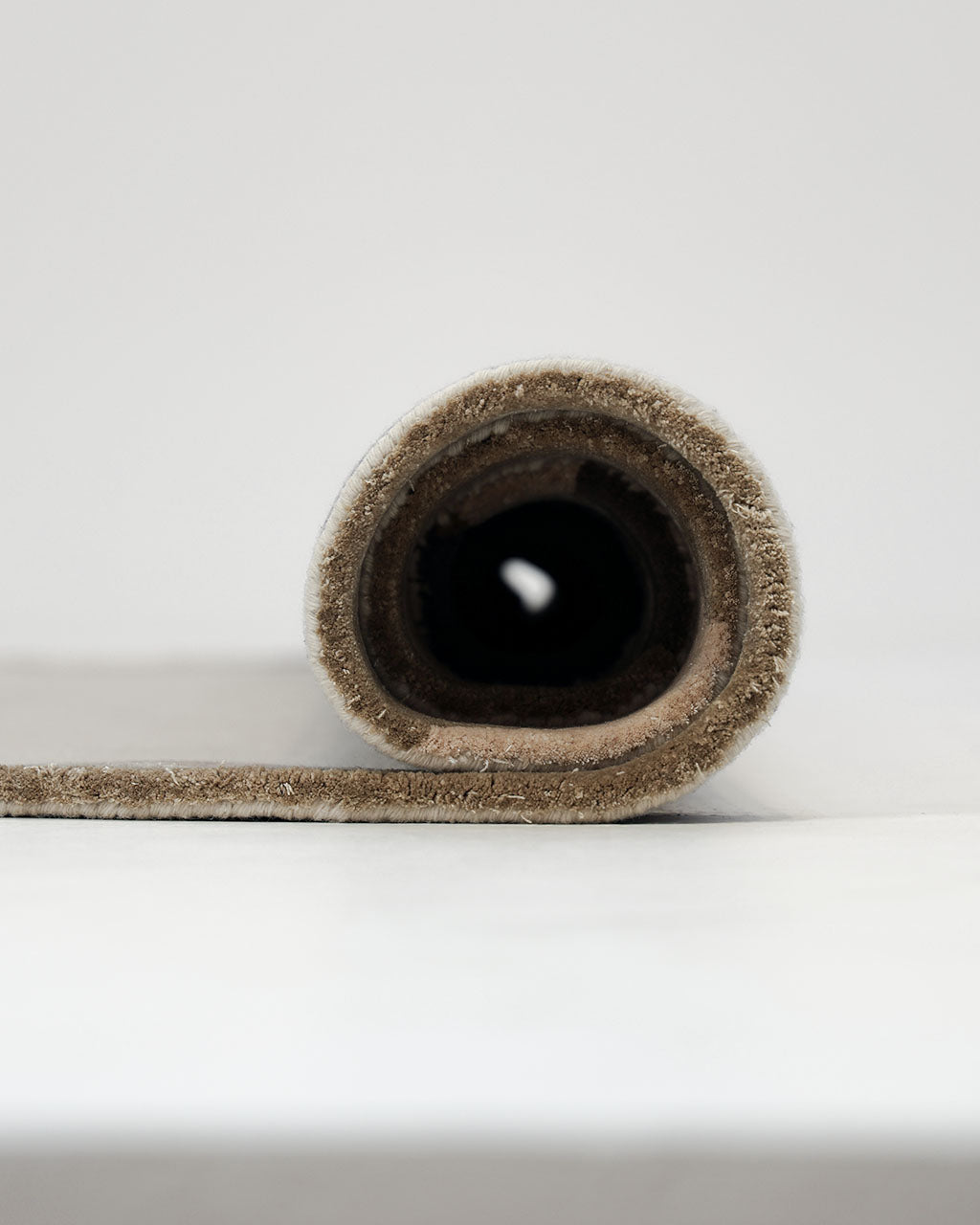 The RAMSHA HOME Terra Eclipse Oval Handmade Rug Accent Rug HTWV-195 in beige is tightly rolled up and placed on a light-colored surface, viewed from the side to showcase the circular pattern of its layers—an elegant accent ideal for any modern interior rug collection.