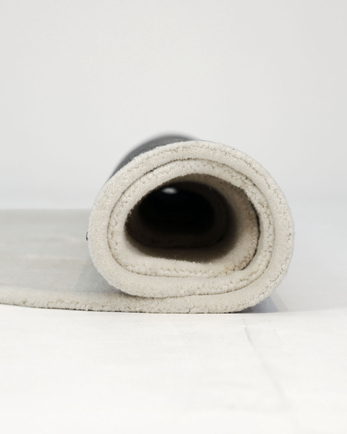 A close-up view of the Stylish Handmade Shape Rug Multi Color HTWV-105 by RAMSHA HOME, rolled up on a white surface, highlighting its soft hand-tufted wool texture and gently rounded edge.