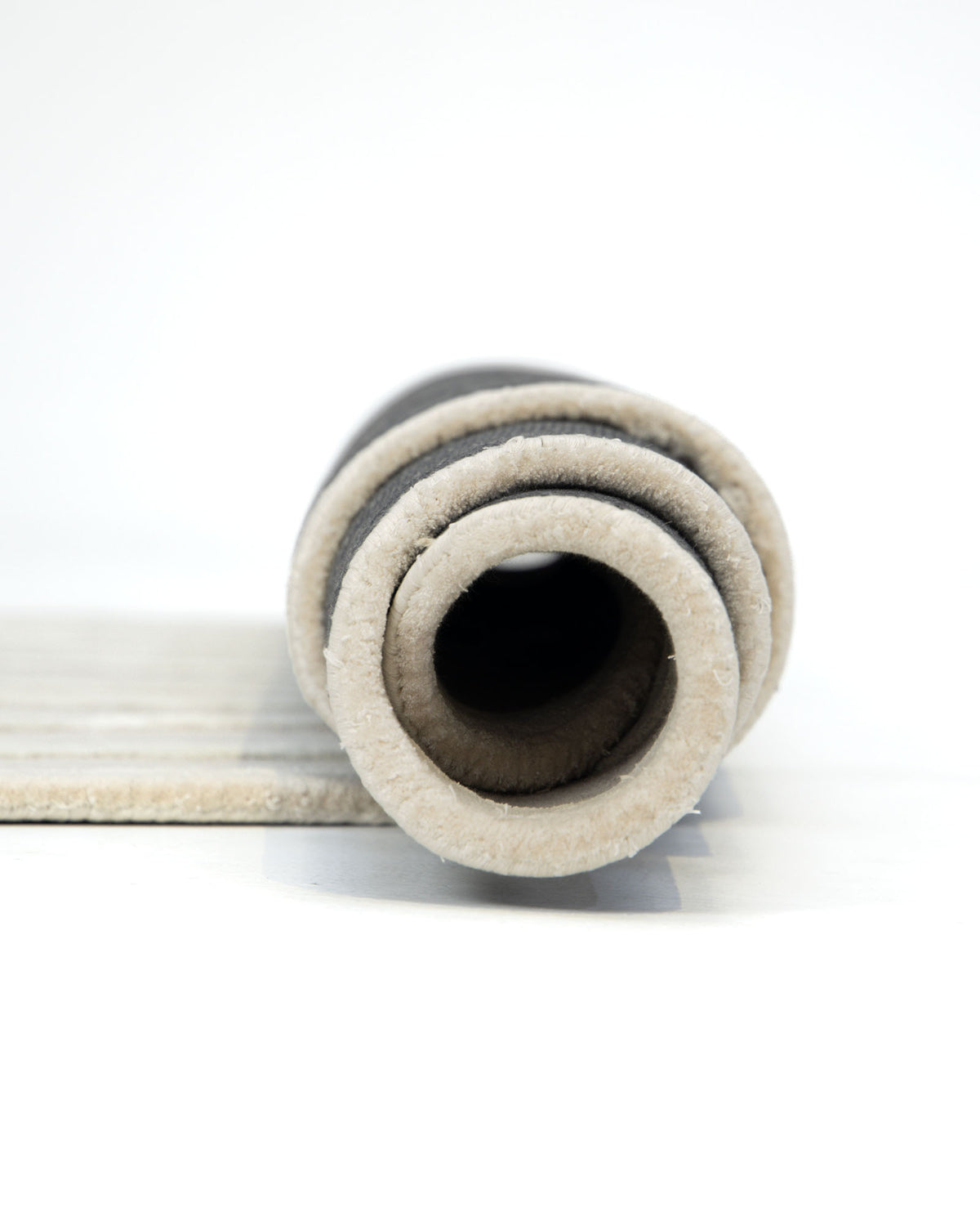 A close-up side view of the RAMSHA HOME Beautiful Off White Handmade Rug - HTWV-112 (200x300cm) shows its plush, hand-tufted layers rolled up on a white surface.