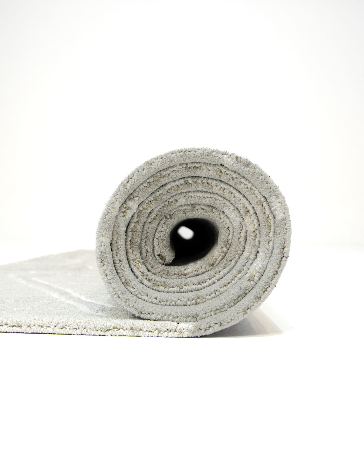 A rolled-up light gray RAMSHA HOME Decorative Rectangle Shape Rug HTP-15 is shown standing on its end against a white background, with the textured material visible in the spiral—its clean lines and subtle texture reminiscent of a modern polyester rug.
