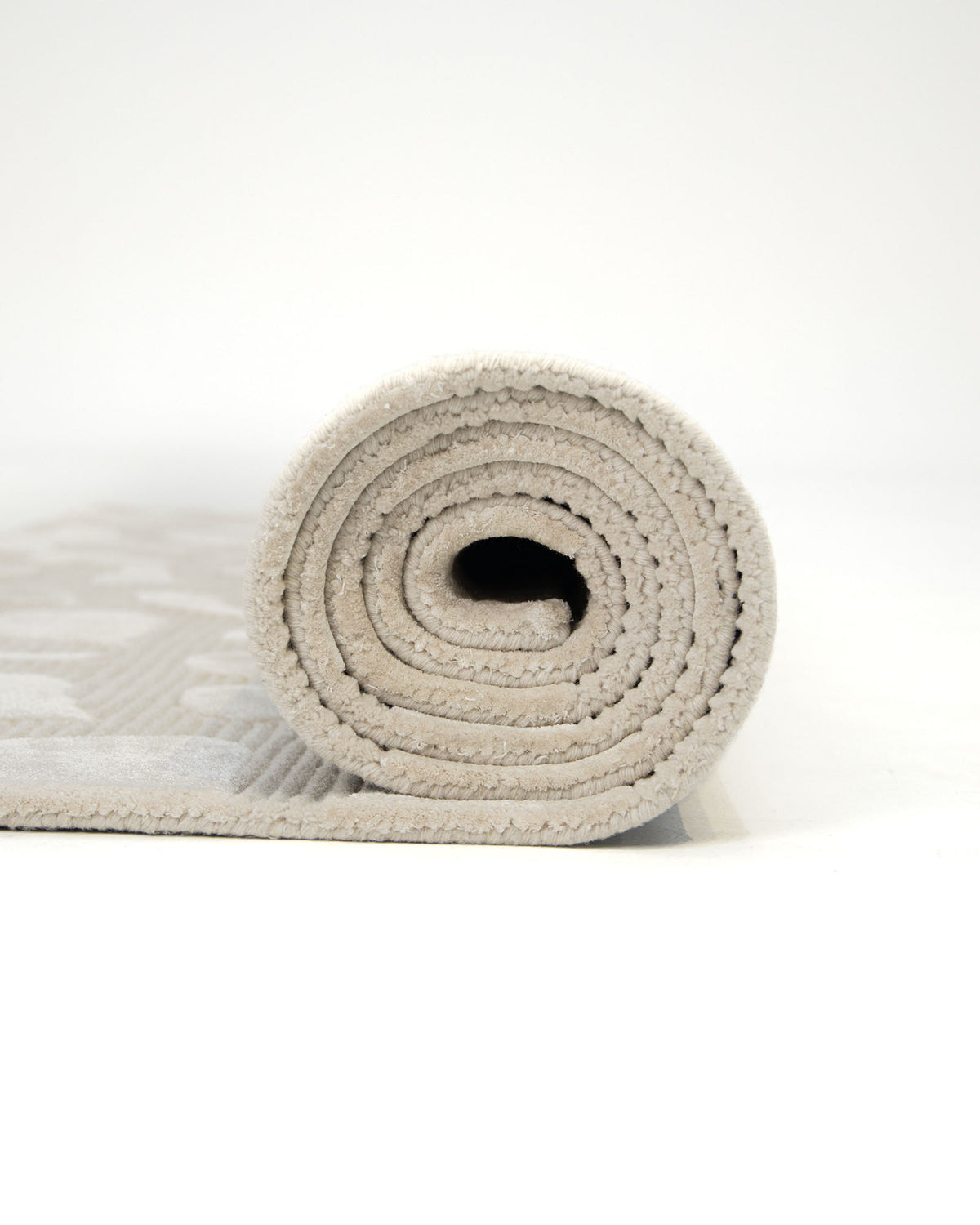A rolled-up RAMSHA HOME Modern Beige Textured Rug (HTWV 203) featuring an abstract organic pattern is placed on a plain white background, highlighting its spiral design from the side.