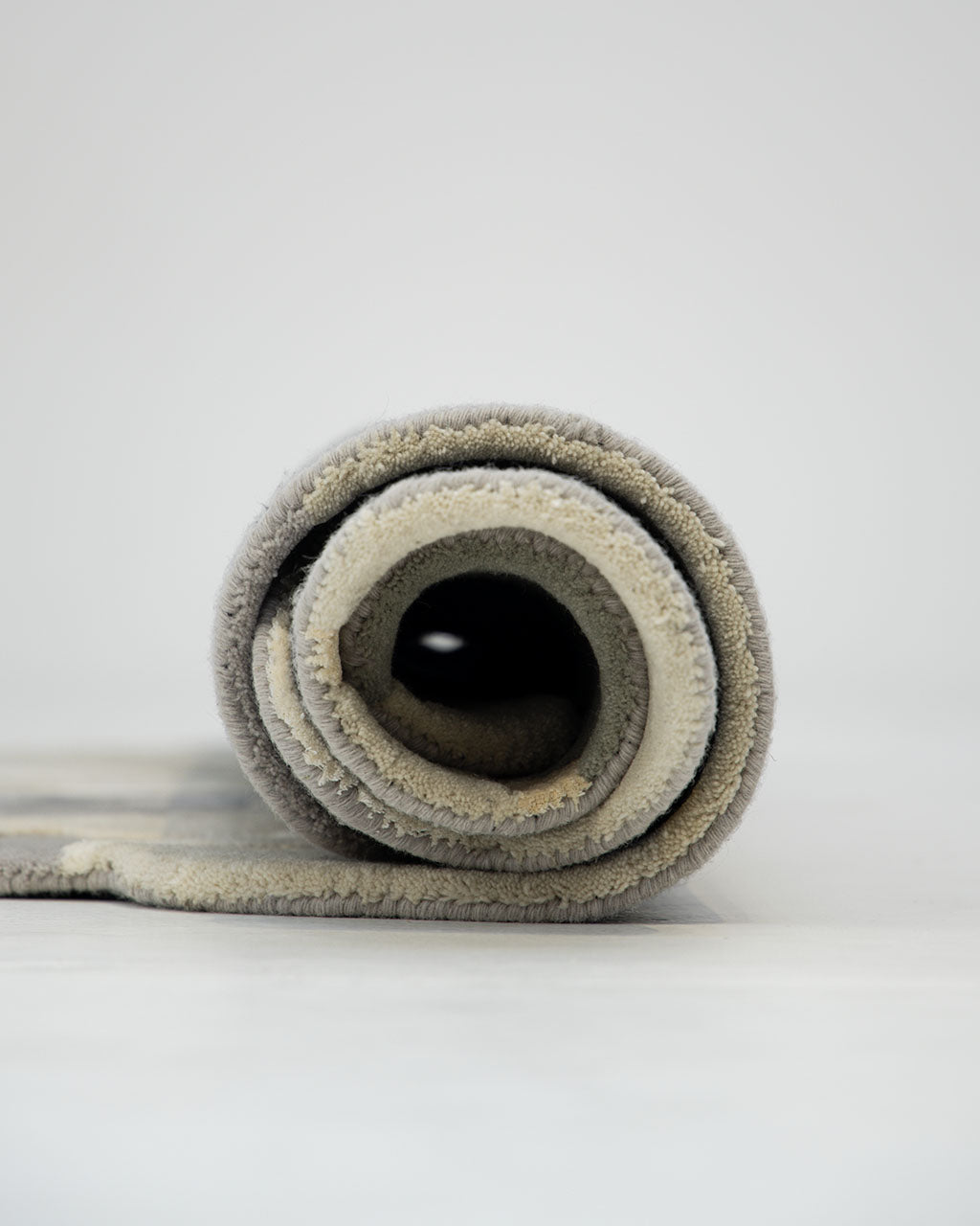 A close-up of the RAMSHA HOME Contemporary Flow Area Handmade Rug HTWV-199, featuring rolled-up beige and gray tones on a light surface, set against a plain light gray background.