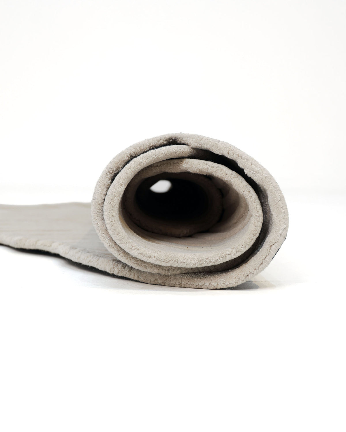 A close-up of a partially unrolled, light gray yoga mat on a white surface reveals circular layers at one end, echoing the graceful patterns of the Organic Shape Flow Line Handmade Area Rug HTWV-141 by RAMSHA HOME.