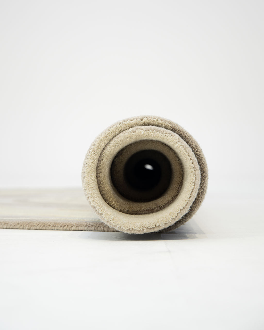 A rolled-up RAMSHA HOME Terra Eclipse Oval Handmade Rug Accent Rug HTW-155 in beige is placed on a light-colored floor, viewed directly from the front to showcase the spiral pattern of the roll.