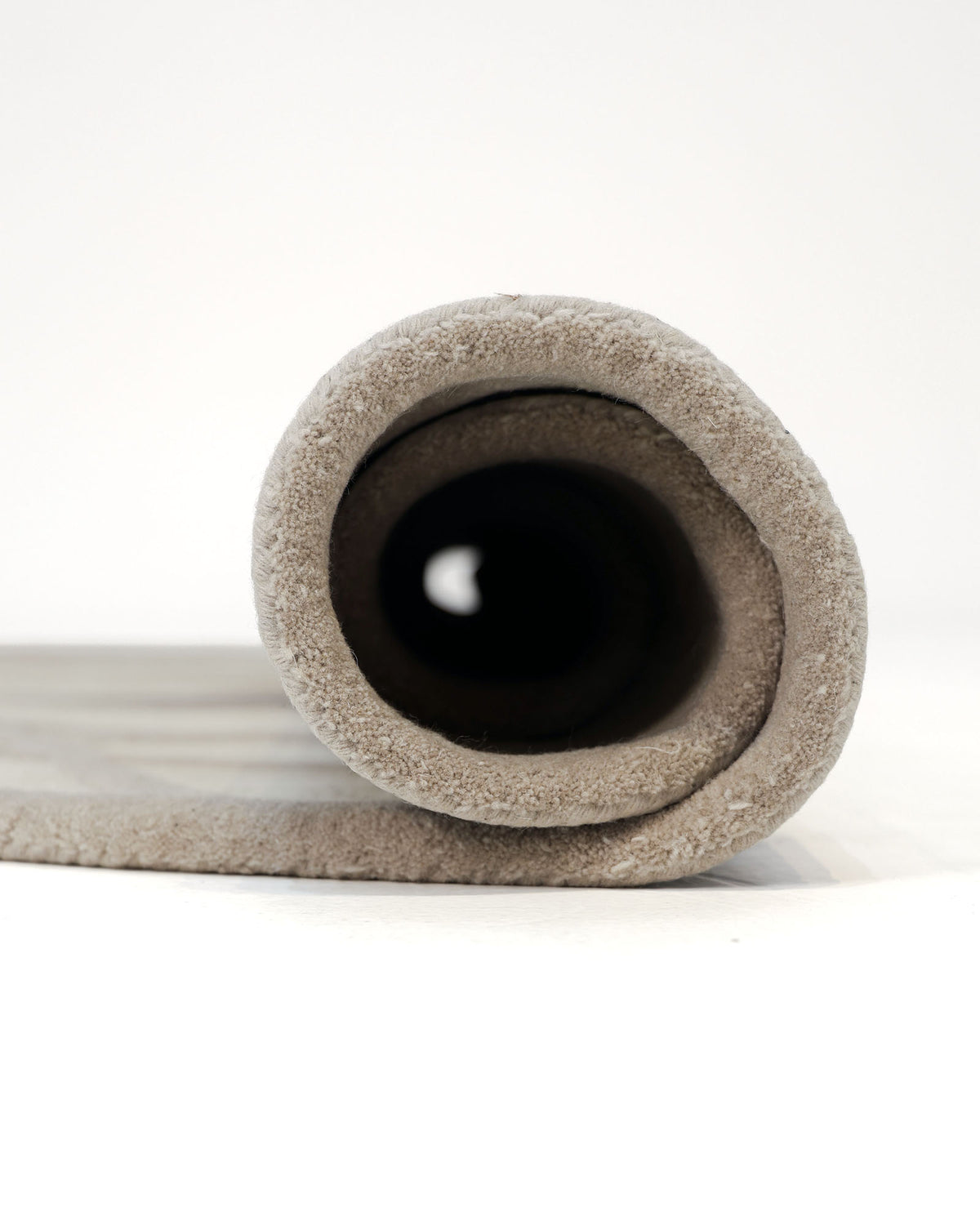 A close-up view of the RAMSHA HOME Geometric Round Handmade Rug 200 cm – HTWV 206 shows the rolled-up beige rug on a white surface, with its circular end facing the camera to highlight its texture and thickness.