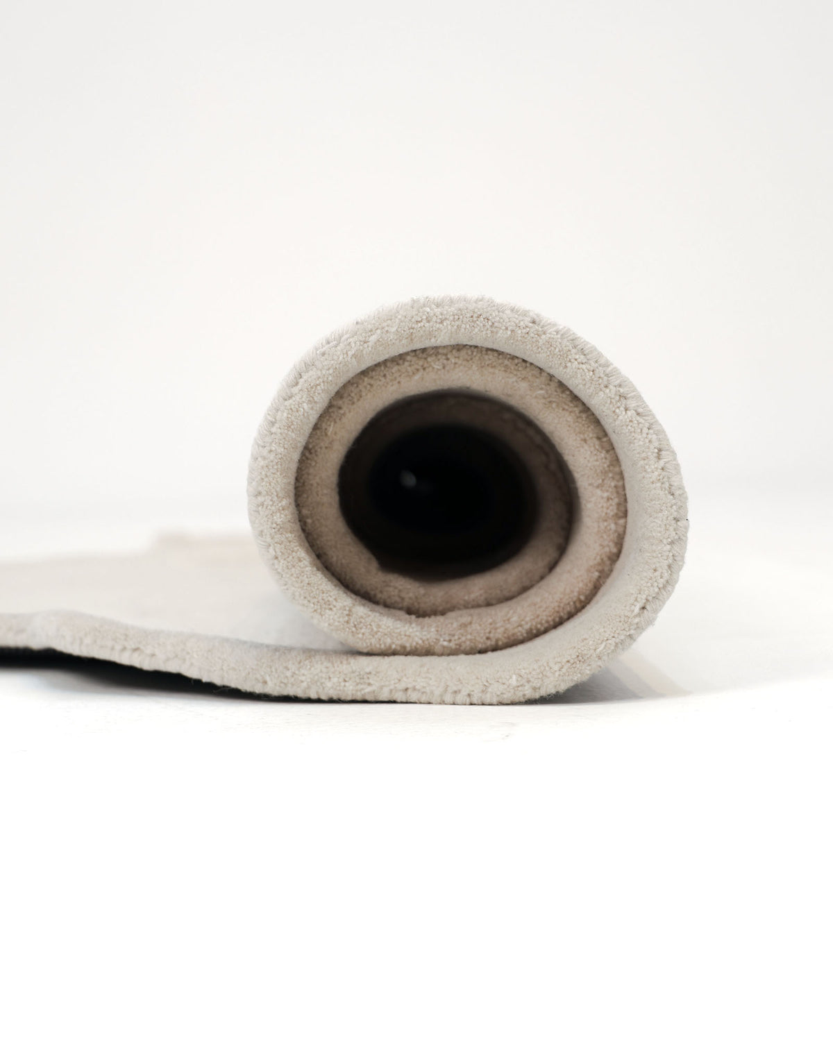 A close-up view of the RAMSHA HOME Modern Sculptural Shape Rug Neutral Beige 200 cm – HTWV 207 rolled up on a white surface, highlighting the spiral pattern of the fabric from the open end.