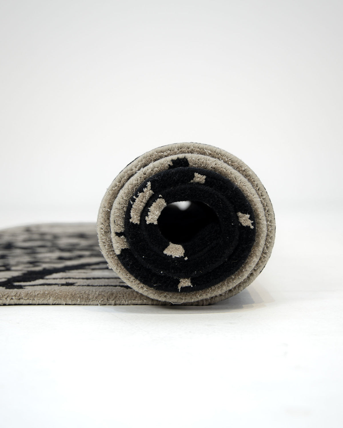 The RAMSHA HOME Abstract Crackle Black & Ivory Rug – HTWV-33, featuring a hand-tufted patterned design in black and ivory, is shown rolled up and viewed from the side against a plain white background.