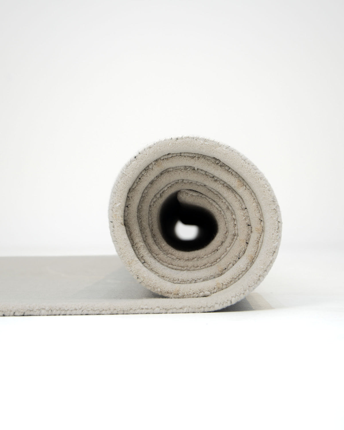 A neatly rolled Embossed Floral Solid Light Grey Rug – HTWV 171 by RAMSHA HOME is viewed from the side against a plain white background, displaying its spiral layers and soft wool viscose texture.