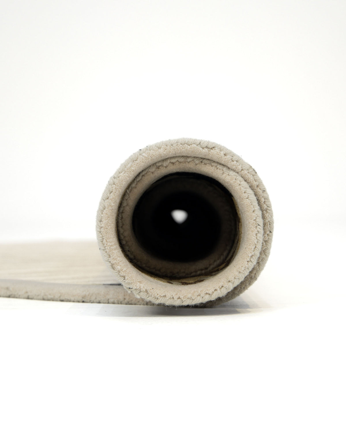 A close-up of the RAMSHA HOME Round Multi Area Rug 200 cm HTW-73, hand-tufted in light beige and rolled up, viewed from one end to highlight its spiral layers and textured edge stitching. The background is plain white.