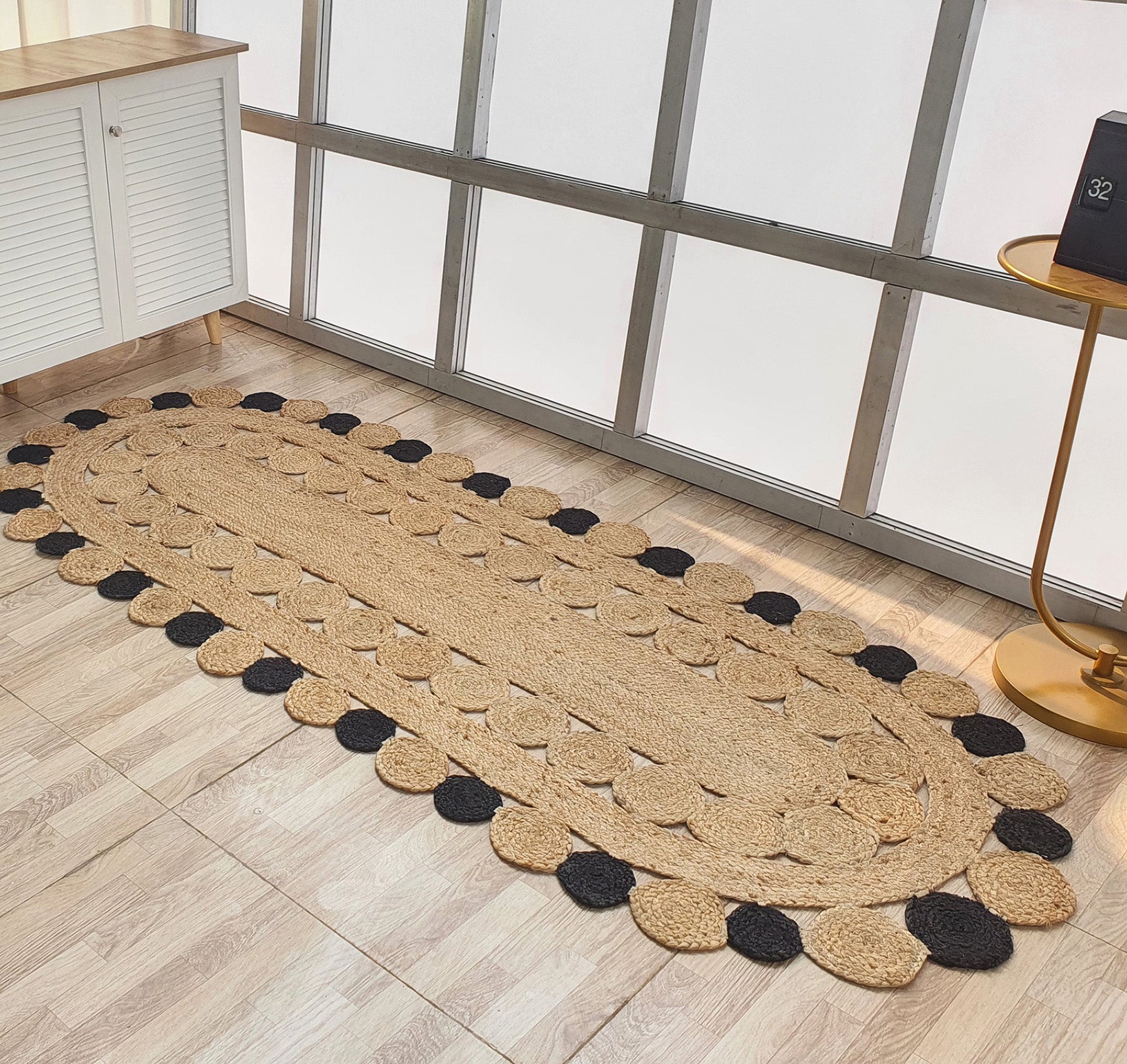 The RAMSHA HOME Oval Shaped Jute Braided Rug Black & Natural BR-033, featuring concentric ovals and alternating tan and black patterns, adds natural texture and beauty to any light wood floor.