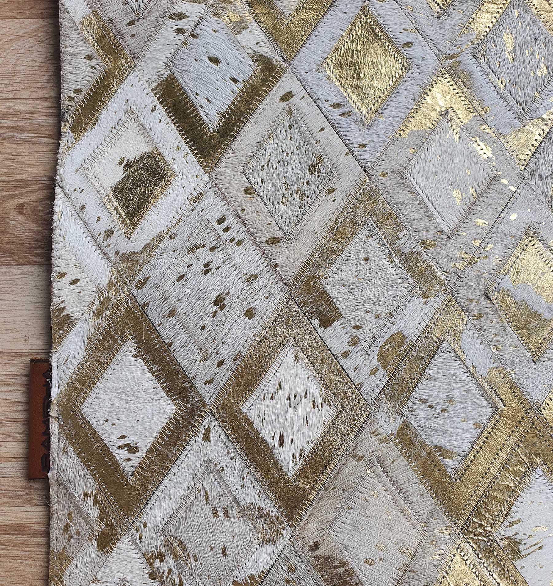 A close-up of the Handmade Diamond Patterned Leather Rug LR-010 by RAMSHA HOME, showcasing white, gold, and beige diamond patterns with a textured look and visible wooden flooring at the edge.