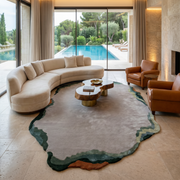 A modern living room with a curved white sofa, two brown leather chairs, a geometric wooden coffee table, and the RAMSHA HOME Handmade Decorative Multi Color Rug HTWV-92, overlooking a pool and garden through floor-to-ceiling windows.