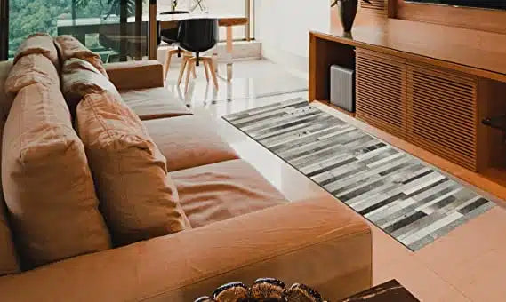 Modern living room with a beige sofa, wooden TV console, and RAMSHA HOME’s Grey Color Kitchen Decor Leather Rug (LR 004). A dining table with two chairs sits by large windows, filling the space with natural light.