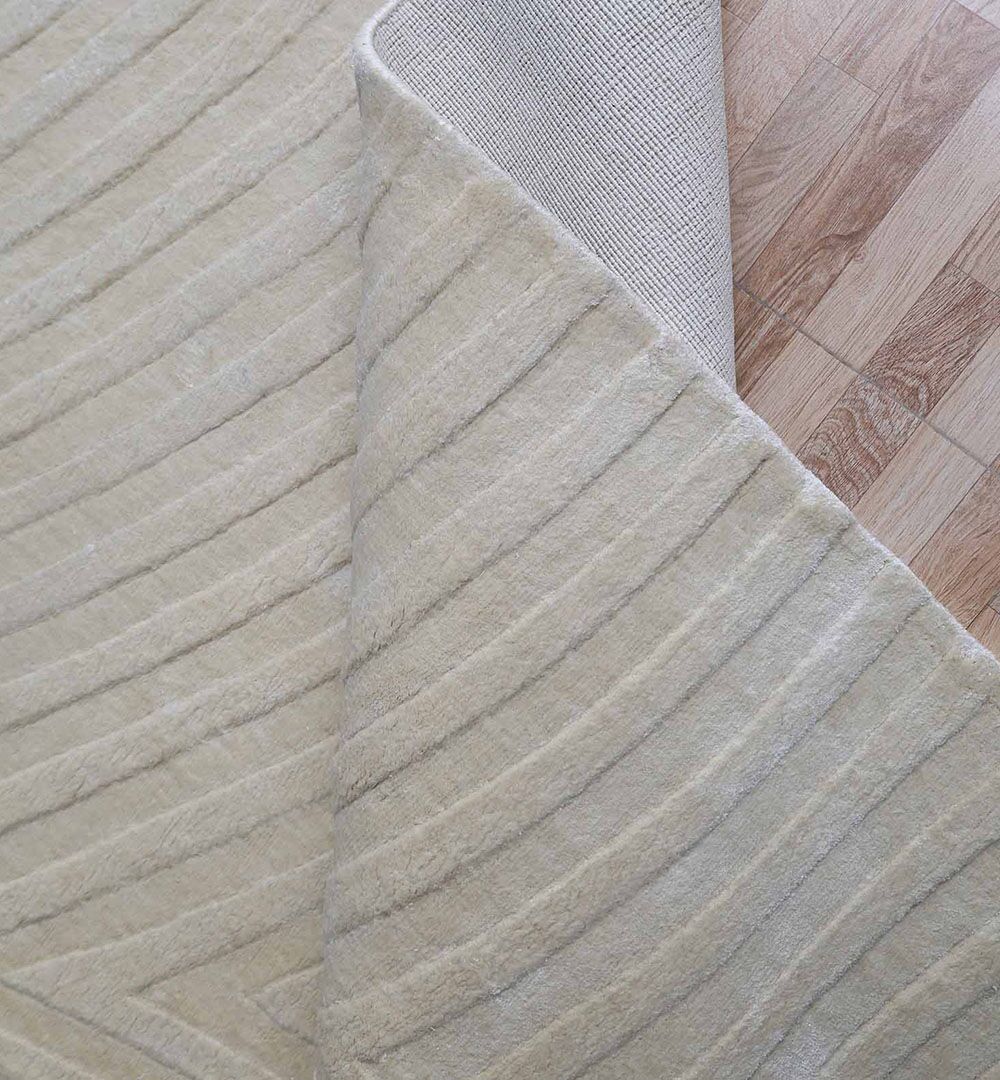 The RAMSHA HOME Vibrant Multi Color Handmade Area Rug - HL 07 is shown with a corner lifted, revealing a light wood floor beneath. The cream-colored rug displays a subtle geometric pattern with raised lines.