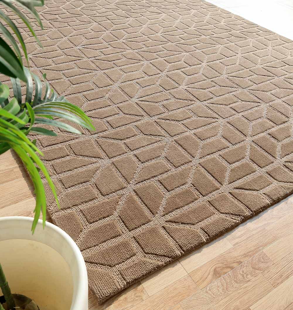 The RAMSHA HOME Drawing Room Decor Novara Rug - CMN 32 (200x290cm) features a taupe geometric diamond and cube pattern on a light wood floor, with a potted green plant in the corner for contrast.