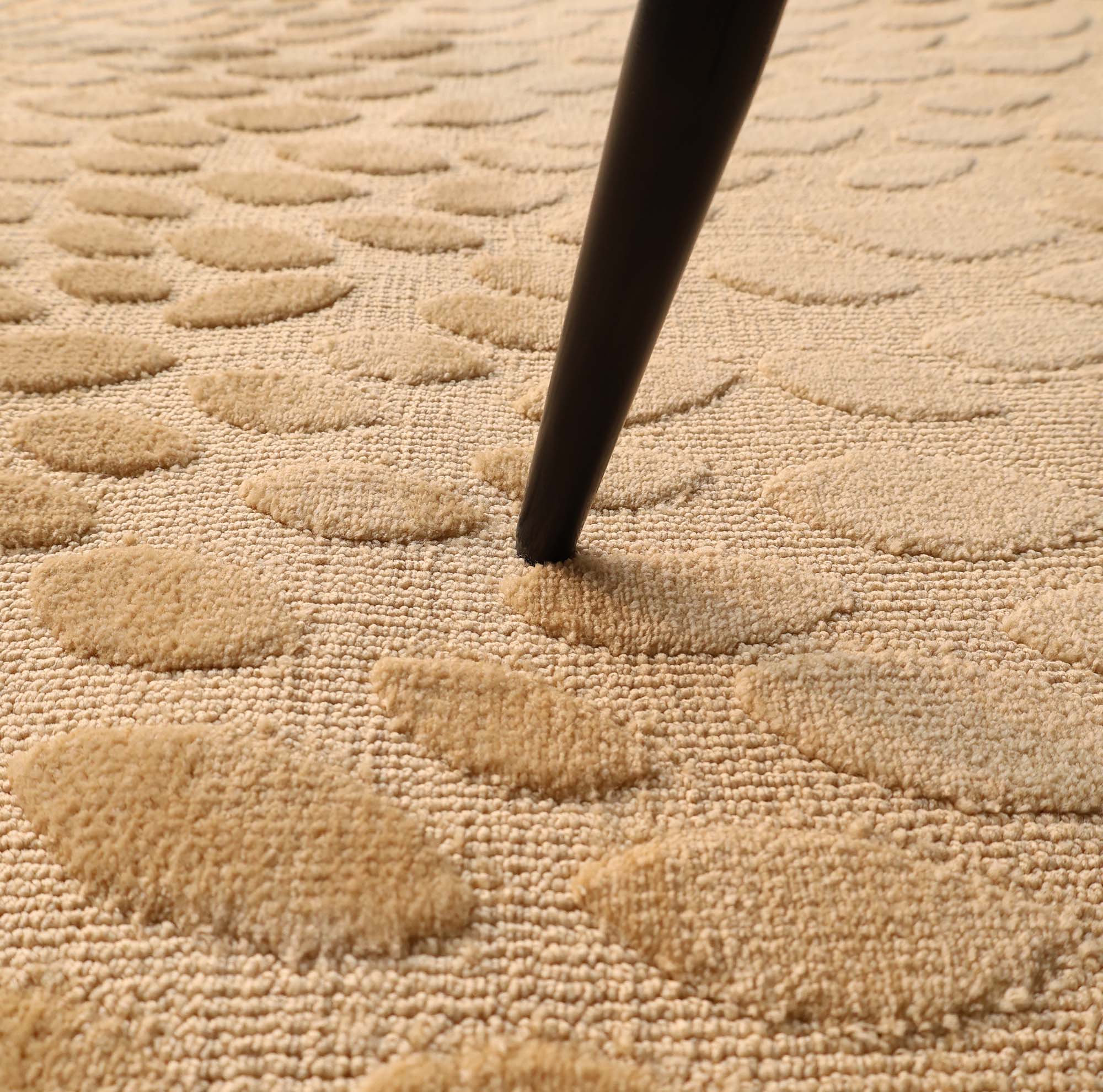 A close-up of the RAMSHA HOME Modern Abstract 200x300 CM Rectangle Shaped Rug CMN 107 in beige, showing its raised oval patterns as a dark wooden furniture leg presses into this handcrafted piece.