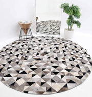 The RAMSHA HOME Multi Color Home Decor Leather Rug - LR 020 featuring black, white, and gray triangles lies on the floor beside a small wooden side table with a magazine, a potted plant, and a tall mirror reflecting the decor.