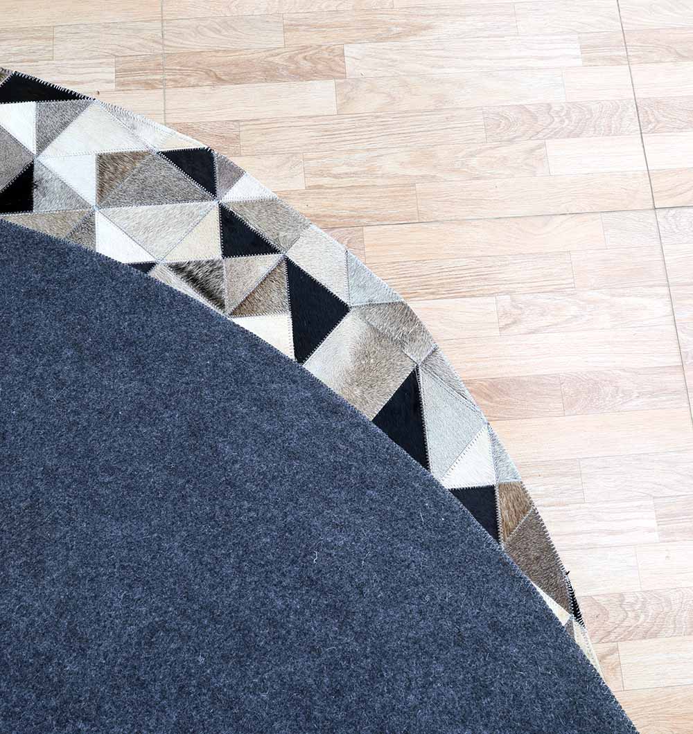 The RAMSHA HOME Multi Color Home Decor Leather Rug - LR 020 features a round design with a dark grey center and a border of beige, brown, black, and white geometric shapes—an eye-catching accent for light wooden floors.