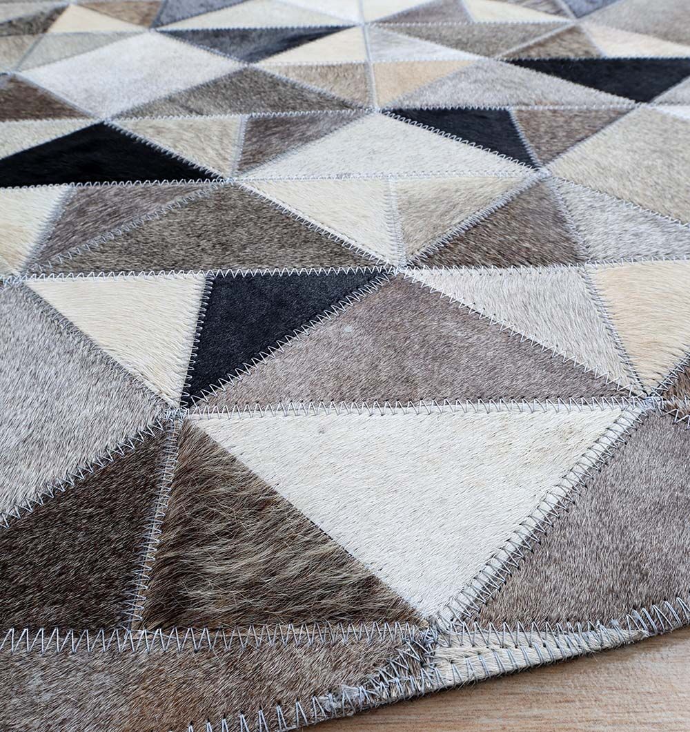 Close-up of the RAMSHA HOME Multi Color Home Decor Leather Rug - LR 020, crafted from triangular cowhide patches in brown, beige, black, and white hues, featuring visible zigzag stitching along the seams.