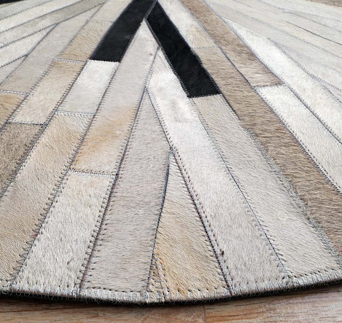 Close-up of the RAMSHA HOME Stunning Multi Color Dining Room Decor Leather Rug - LR 021, crafted from stitched animal hide strips in beige, cream, brown, and black chevrons, displayed on a wooden floor.