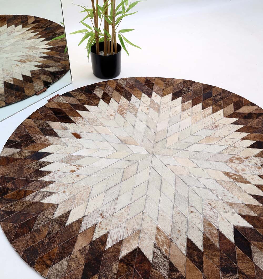 The RAMSHA HOME Multi Color Guest Room Round Decor Leather Rug - LR 022, featuring a geometric starburst pattern in brown and cream, is shown on a white floor next to a green potted plant and a mirror reflecting the rug.