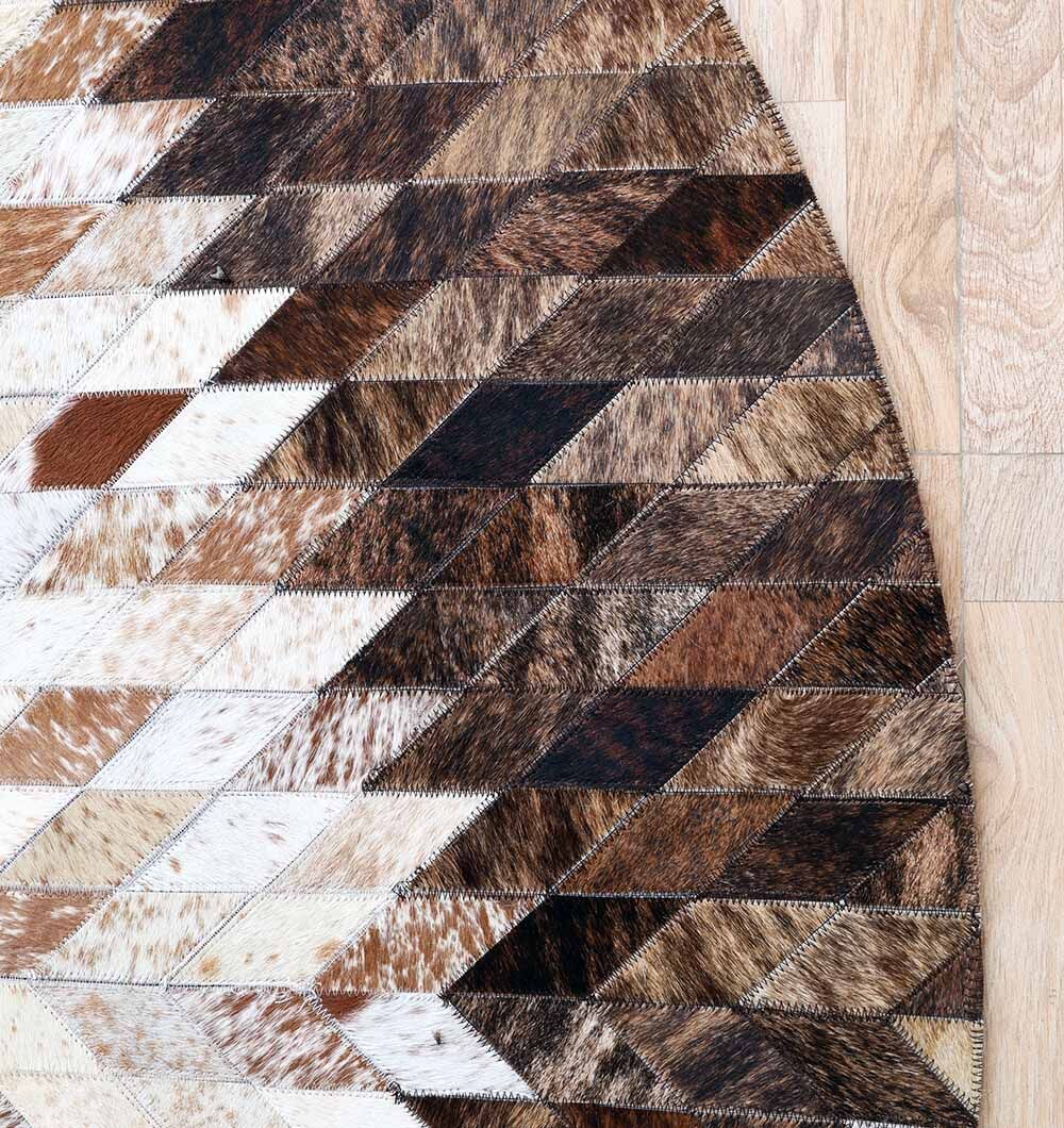 The RAMSHA HOME Multi Color Guest Room Round Decor Leather Rug - LR 022, featuring a starburst pattern in brown, white, and black leather pieces, adds elegance to light-toned wooden floors.