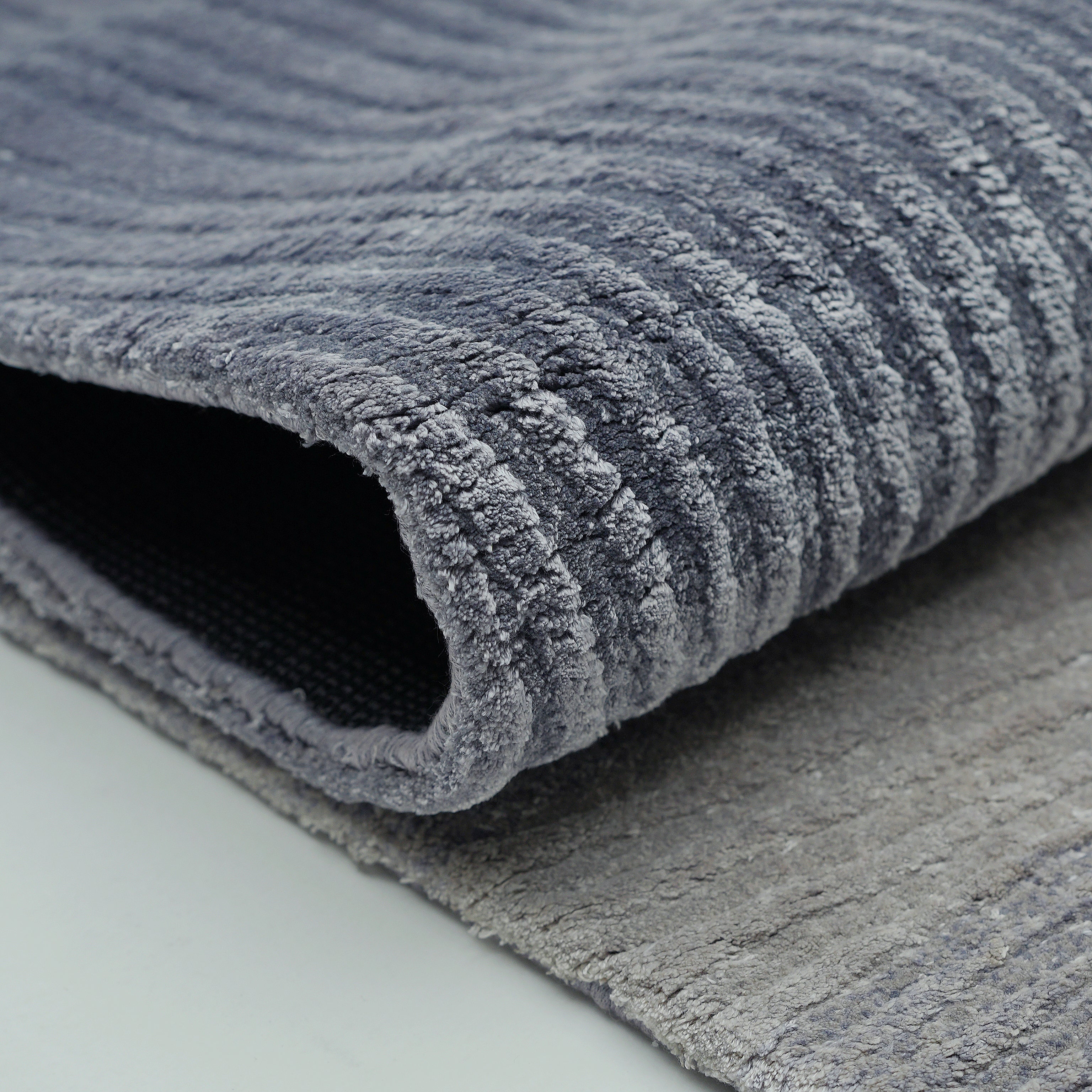 Close-up of the Blue Ginkgo Fan Handmade Rug HTV 29 by RAMSHA HOME (300x400 cm), featuring textured, ribbed lines and soft Tencel cotton fabric. The plush gray rug's backing is partially visible as it rests on a light surface.