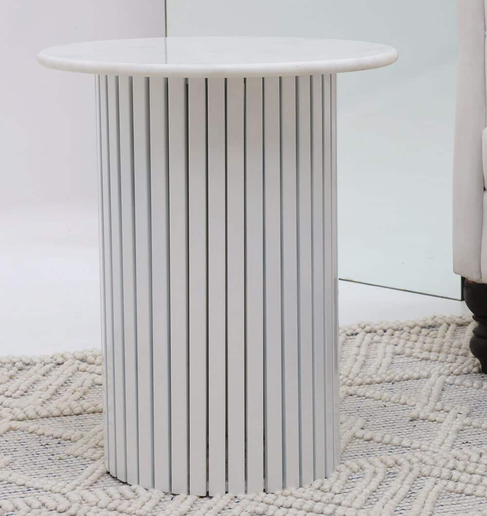 The RAMSHA HOME Modern White Marble Center Table AD23-12, featuring a round top and vertical stripe details on its cylindrical base, is placed on a textured woven rug beside a white upholstered chair.