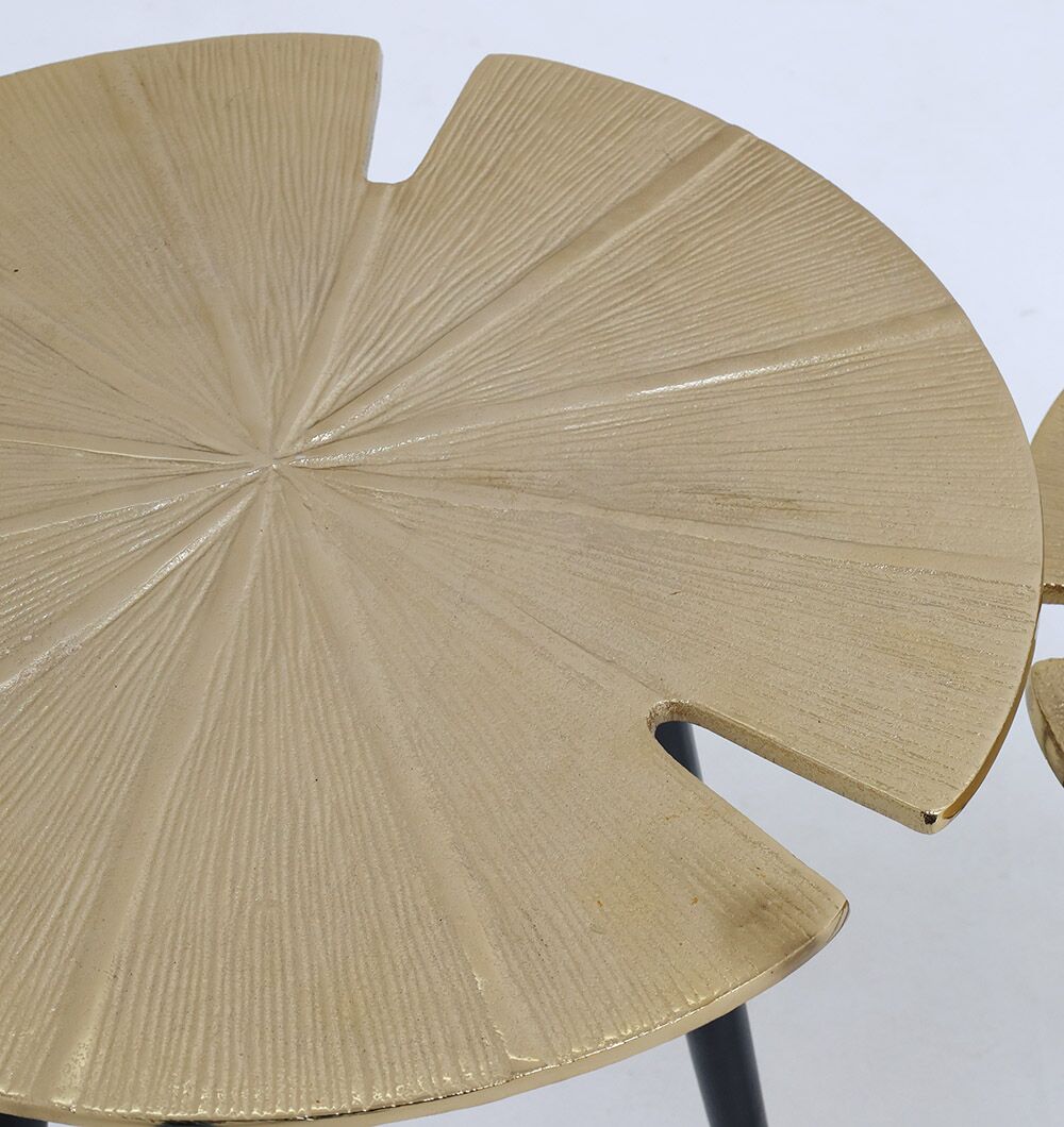 Close-up of a round, gold-toned tabletop with a lily pad–inspired pattern, part of the Lily Luxe Aluminum Accent Tables – Set of 2 Nesting Tables from RAMSHA HOME’s modern black and gold collection. Contrasting black legs complete the elegant look.