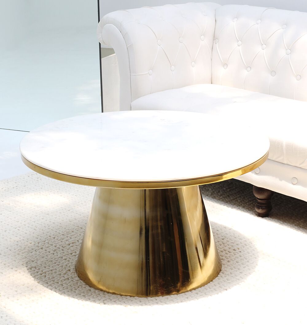 The Aurelia Luxe Marble & Iron Accent Table by RAMSHA HOME, featuring a white marble top and gold cone-shaped base, sits on a textured beige rug beside a white tufted sofa.