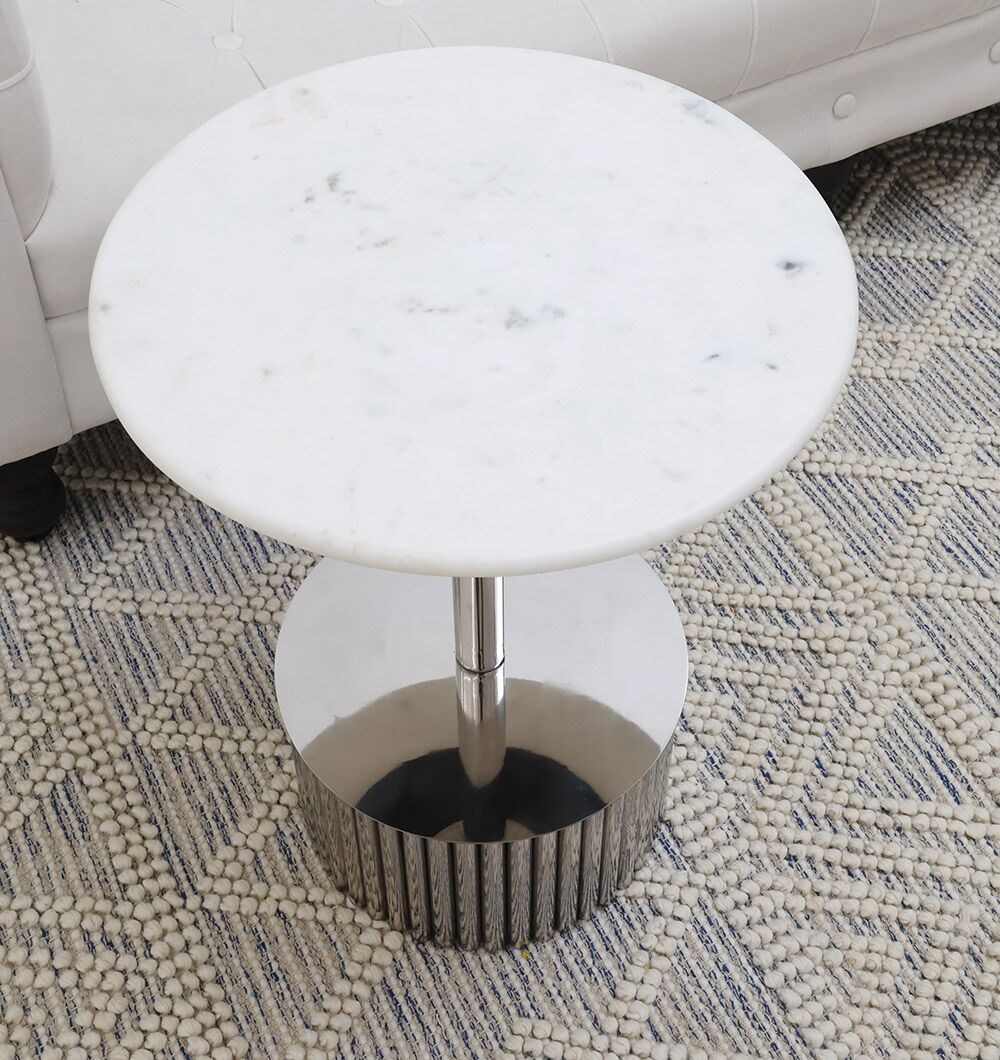 The RAMSHA HOME Luna Polished Marble & Steel Side Table features a small round white marble top and shiny silver metal base, adding modern elegance to any space when placed on a patterned rug beside a white upholstered sofa.