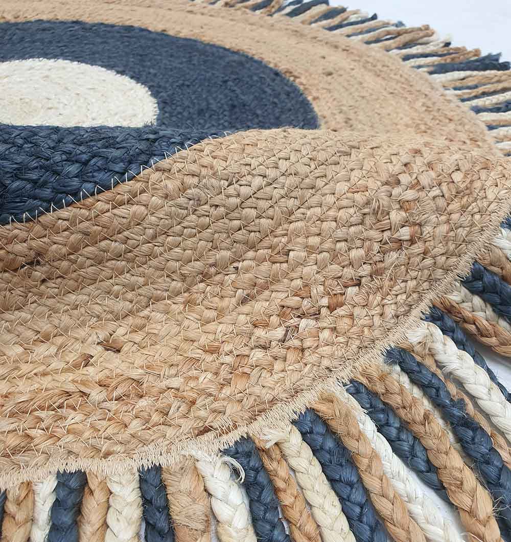 A close-up of the RAMSHA HOME Amazing Handmade Braided Round Jute Rug - BR 001, featuring a spiral pattern in natural, cream, and dark blue with braided fringe in alternating blue, beige, and white—perfect as a stylish accent for any room.