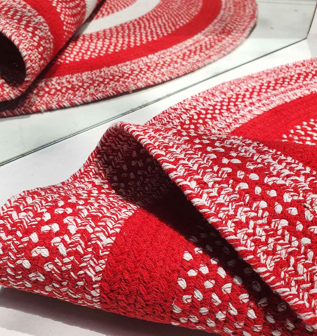 A close-up of the RAMSHA HOME Red & White Color Round Braided Rug - BR 005 on a white surface, with part of the rug folded and its reflection visible in a nearby mirror.