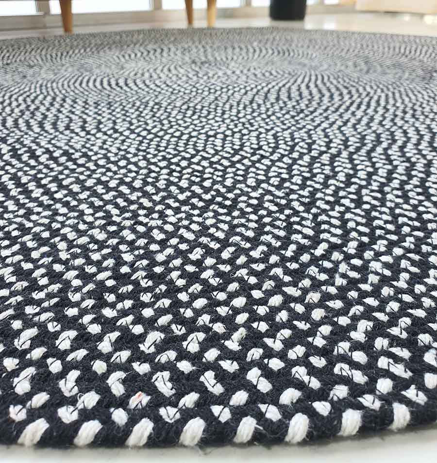 Close-up of the RAMSHA HOME Black & White Color Round Braided Rug - BR 007 on the floor, featuring visible textured patterns and woven details, with furniture legs in the background.