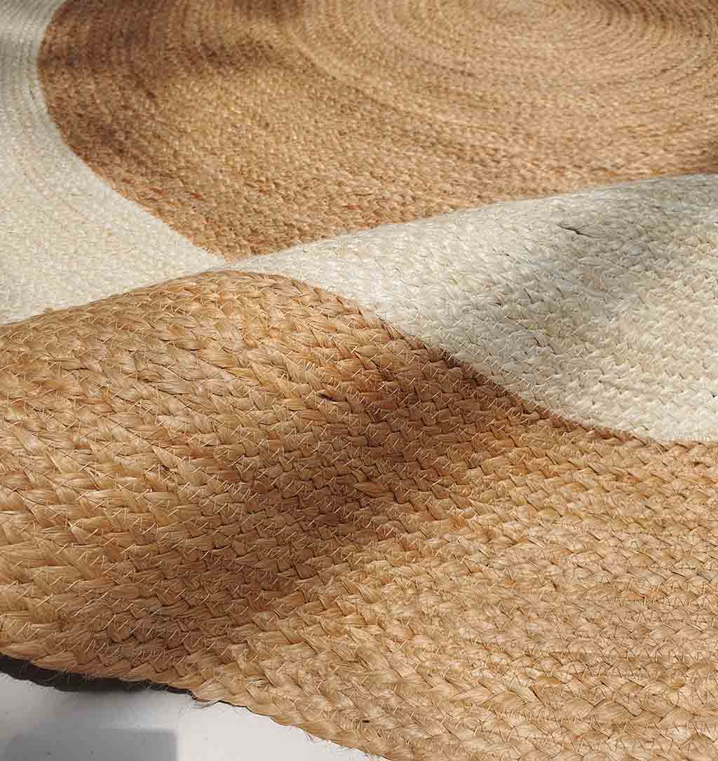 A close-up of the RAMSHA HOME Jute Rug Natural And Bleach Round Carpet BR-008 highlights its braided jute texture with natural beige and white sections, and a gentle fold that creates shadow and depth.