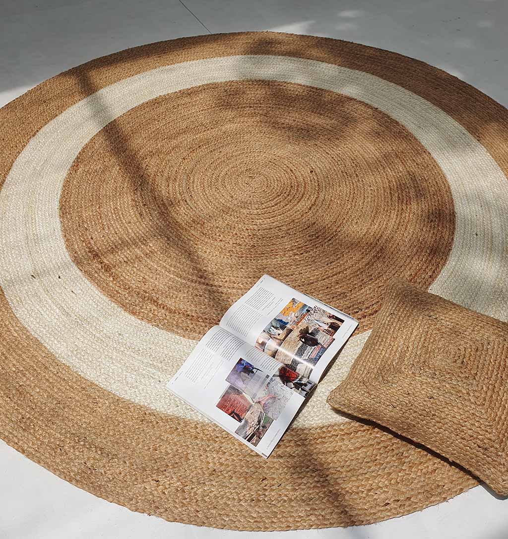The RAMSHA HOME Jute Rug Natural And Bleach Round Carpet BR-008, paired with an open book and a square jute pillow, creates a cozy and inviting space.