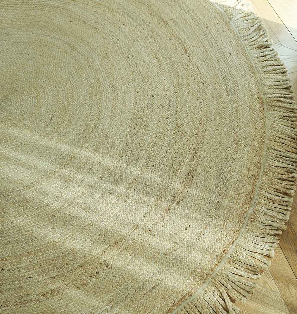 A close-up of RAMSHA HOME’s Natural Jute Braided Rug With Fringes BR-015 on a wooden floor, sunlight enhancing its circular pattern, natural texture, and boho style.