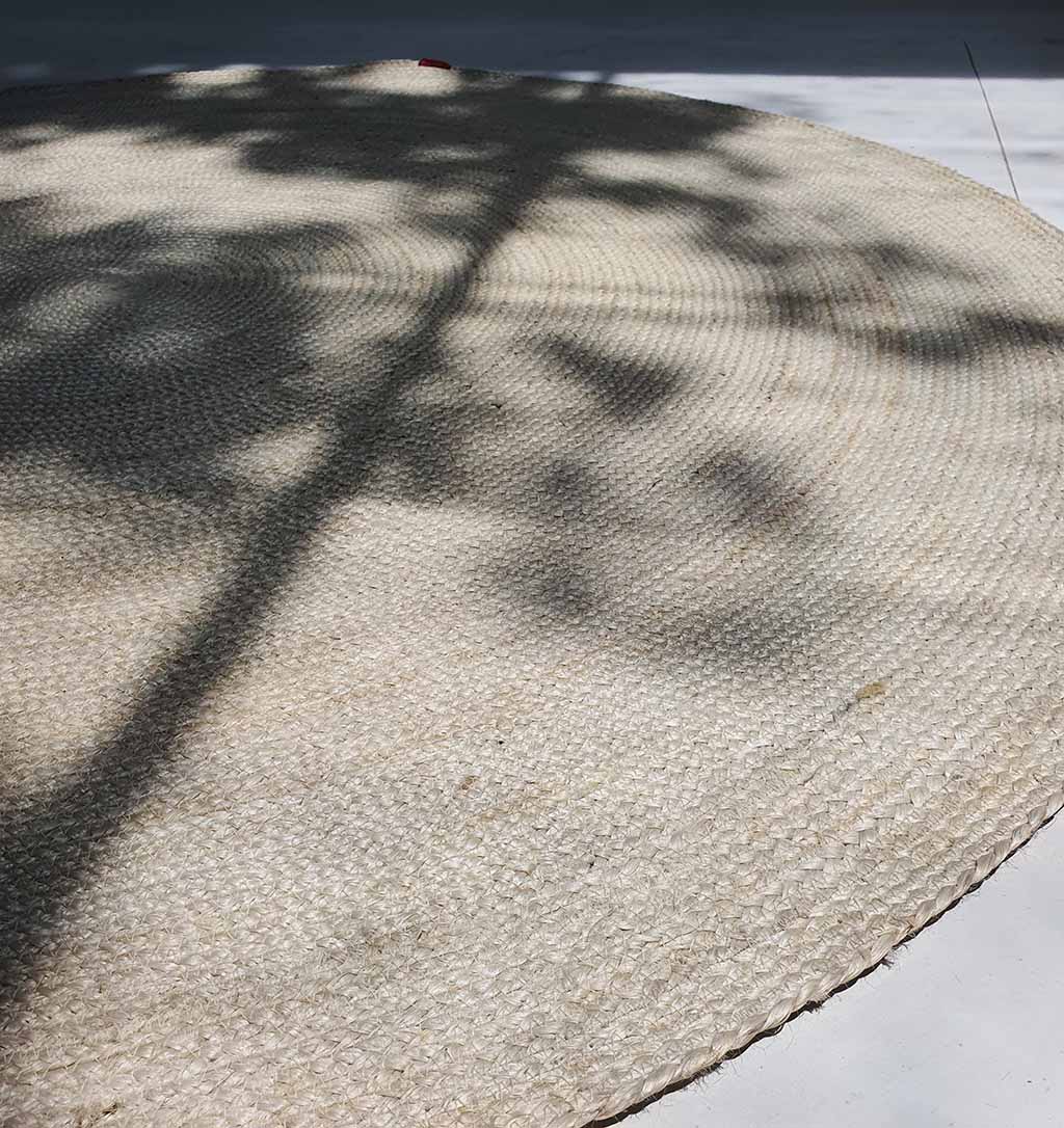 The Natural Jute Rug Bleach Color BR-017 rests on a light floor, its woven beige surface illuminated by soft shadows—a perfect neutral area rug to bring calm to any space.